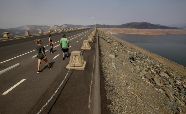 FILE - In this Sunday, Aug. 22, 2021 file photo, pedestrians walk across Oroville Dam at Lake Oroville State Recreation Area as drought conditions continue in Butte County, Calif. Severe drought across the West drained reservoirs this year, slashing hydropower production and further stressing the region’s power grids. And as extreme weather becomes more common with climate change, grid operators are adapting to swings in hydropower generation. (AP Photo/Ethan Swope)