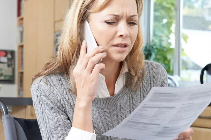 A woman in a wheelchair making a phone call while reading official documents