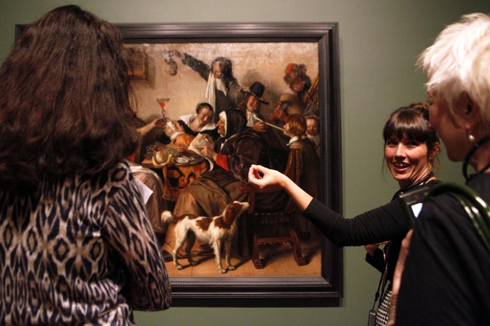 This June 19, 2013 photo shows Nicole Cromartie, coordinator of museum interpretation at the High Museum of Art, speaking with visitors about Jan Steen's painting "As the Old Sing, So Twitter the Young" on display in the "Girl with a Pearl Earring: Dutch Paintings from the Mauritshuis" exhibit during a media preview at the museum in Atlanta. The exhibit, which opens Sunday and runs through Sept. 29, includes Johannes Vermeer’s famous “Girl With a Pearl Earring" painting and 34 other works from the Dutch Golden Age. (AP Photo/Jaime Henry-White)