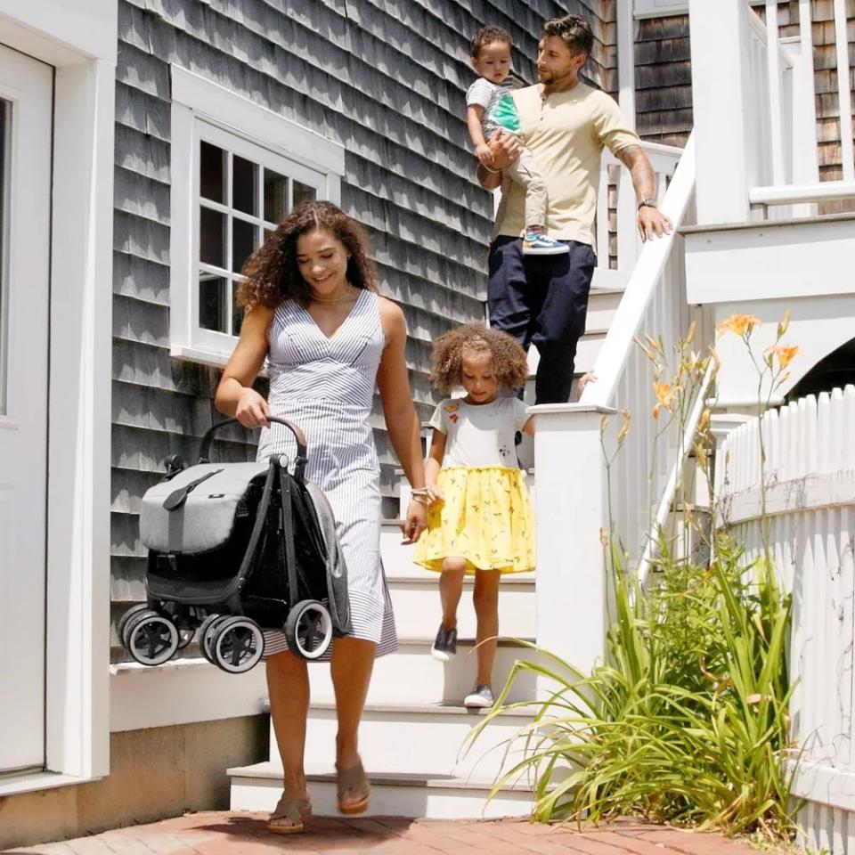 Model holding gray and black stroller folded and walking with children down a set of stairs