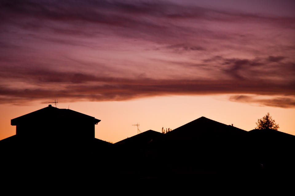 Silhouettes of the roofline of suburban houses at sunset.