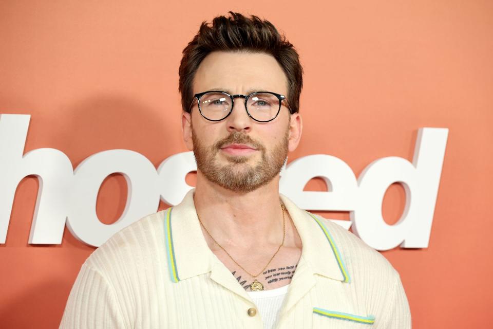 a close-up of Chris Evans at a film premiere, wearing a cream shirt and glasses