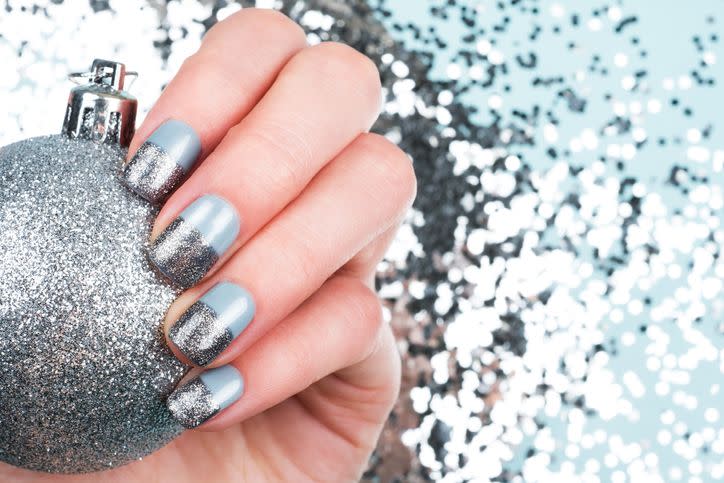 woman hand with baubles and festive glitter manicure on blue shiny background christmas holiday concept