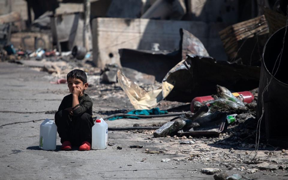 A boy with two water canisters next to destroyed shelters in Moria camp - Reuters