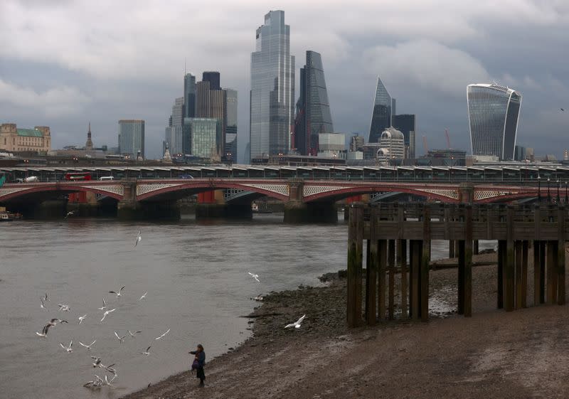 A woman feeds birds on the bank of the river Thames with London's financial district seen in the background, amid the coronavirus disease (COVID-19) in London