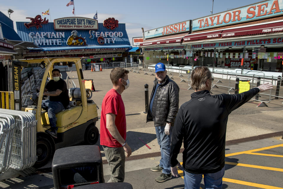 In this April 6, 2020, photo, Billy White, right, and his brother Sonny White, second from right, owners of Captain White Seafood City, along with their nephew Paul White, left, and Stan Kiser with Jessie Taylor Seafood, second from left, set up portable fencing in the hope to force customers to social distance at the Fish Market at The Wharf in Washington. The Fish Market was closed by city officials over the weekend after large crowds gathered. The officials said the market may be allowed to reopen if they can show a plan for safe social distancing. (AP Photo/Andrew Harnik)