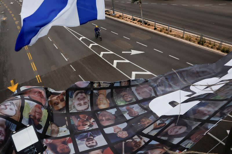 FILE PHOTO: A cyclist rides underneath an Israeli flag and a banner hanging from a bridge with photos of the hostages kidnapped in the deadly October 7 attack on Israel, in Tel Aviv