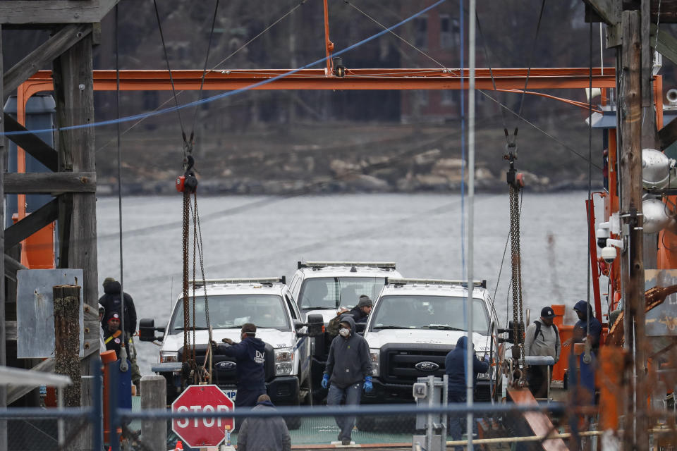 A half-dozen workers, one in a mask, sail back to the mainland aboard a ferry carrying white New York City Department of Corrections vans. 