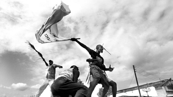 A Sierra Leonean flies a peace flag while standing on a truck