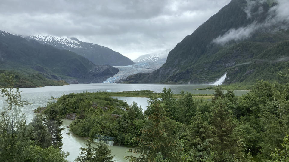 The Mendenhall Glacier, rear, is seen from the glacier visitor center, on June 30, 2023, in Juneau, Alaska. Pictured at right is Nugget Falls. Estimates suggest that by 2050, the glacier may not be visible from the visitor center. As the Mendenhall Glacier continues to recede, tourists are flooding into Juneau. A record number of cruise ship passengers are expected this year in the city of about 30,000 people. (AP Photo/Becky Bohrer)