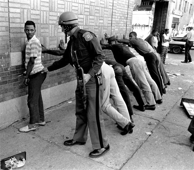 FILE - In this July 24, 1967 file photo, a Michigan State police officer searches a youth on Detroit's 12th Street where looting was still in progress after the previous day's rioting. The last surviving member of the Kerner Commission says he remains haunted that the panel's recommendations on US race relation and poverty were never adopted, but he is hopeful they will be one day. Former U.S. Sen. Fred Harris says 50 years after working on a report to examine the causes of the late 1960s race riots he strongly feels that poverty and structural racism still enflames racial tensions even as the United States becomes more diverse. (AP Photo/File)