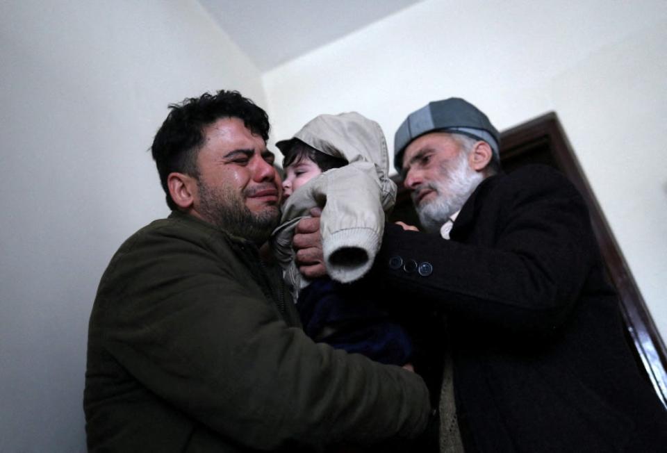 Hamid Safi llora mientras carga a Sohail y se lo entrega a su abuelo Mohammad Qasem Razawi en Kabul (REUTERS)