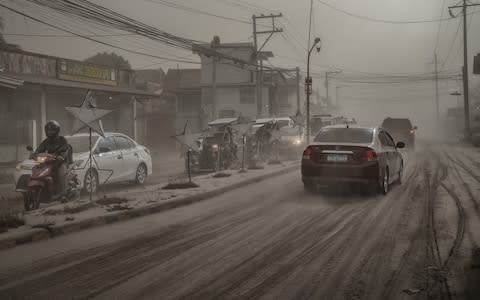Residents in the town of Lemery attempt to carry on with everyday life as ash carpets the streets - Credit: Ezra Acayan/Getty Images