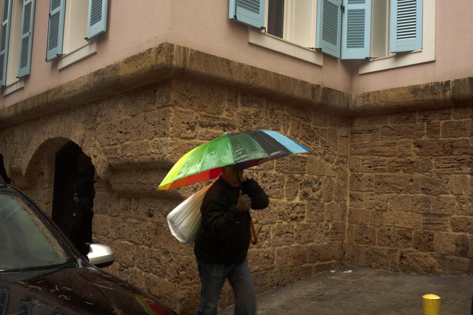 A man walks with an umbrella past the house of ex-Nissan chief Carlos Ghosn in Beirut, Lebanon, Friday, Jan. 3, 2020. The former Nissan Motor Co. Chairman fled Japan this week while awaiting trial on financial misconduct charges and appeared in Lebanon. (AP Photo/Maya Alleruzzo)