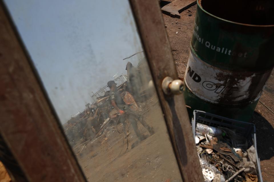 A worker is reflected in a mirror of a destroyed wooden yacht on Salamina island, west of Athens, on Wednesday, July 1, 2020. Greece this year is commemorating one of the greatest naval battles in ancient history at Salamis, where the invading Persian navy suffered a heavy defeat 2,500 years ago. But before the celebrations can start in earnest, authorities and private donors are leaning into a massive decluttering operation. They are clearing the coastline of dozens of sunken and partially sunken cargo ships, sailboats and other abandoned vessels. (AP Photo/Thanassis Stavrakis)