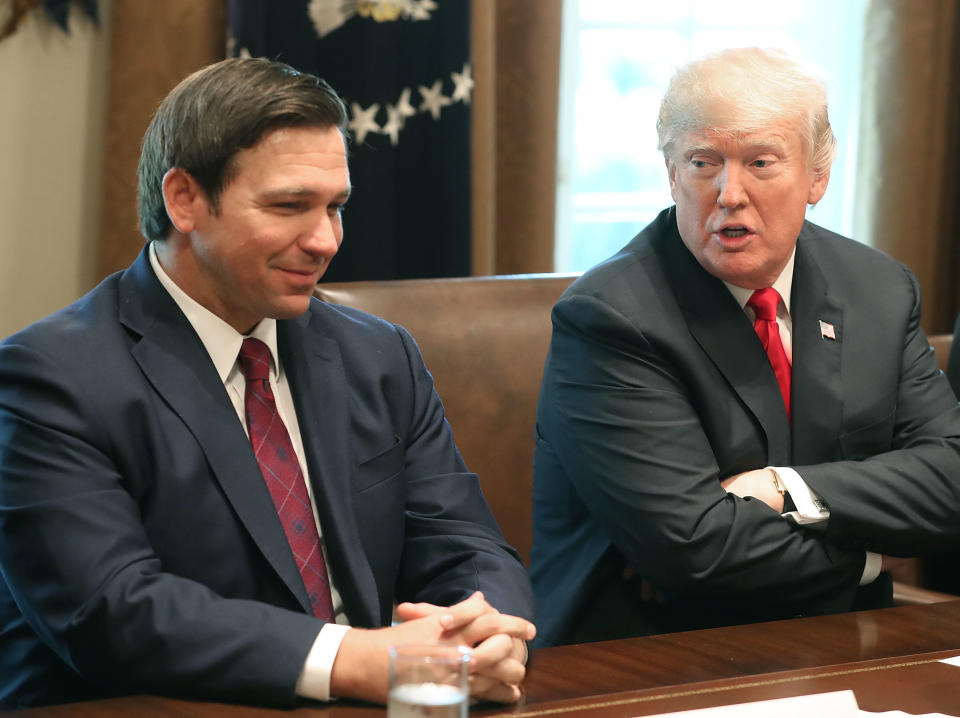 Ron DeSantis smiles while sitting next to Trump, who appears to be speaking to him, at a table.