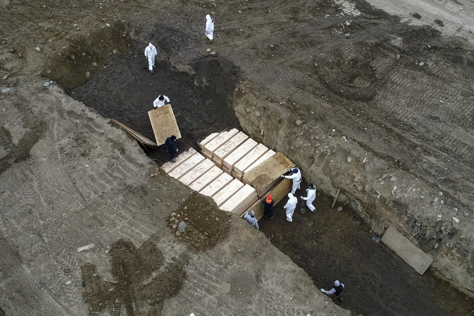 Workers wearing personal protective equipment bury bodies in a trench on Hart Island, Thursday, April 9, 2020, in the Bronx borough of New York. On Thursday, New York City’s medical examiner confirmed that the city has shortened the amount of time it will hold on to remains to 14 days from 30 days before they will be transferred for temporary internment at a City Cemetery. Earlier in the week, Mayor Bill DeBlasio said that officials have explored the possibility of temporary burials on Hart Island, a strip of land in Long Island Sound that has long served as the city’s potter’s field. (AP Photo/John Minchillo)