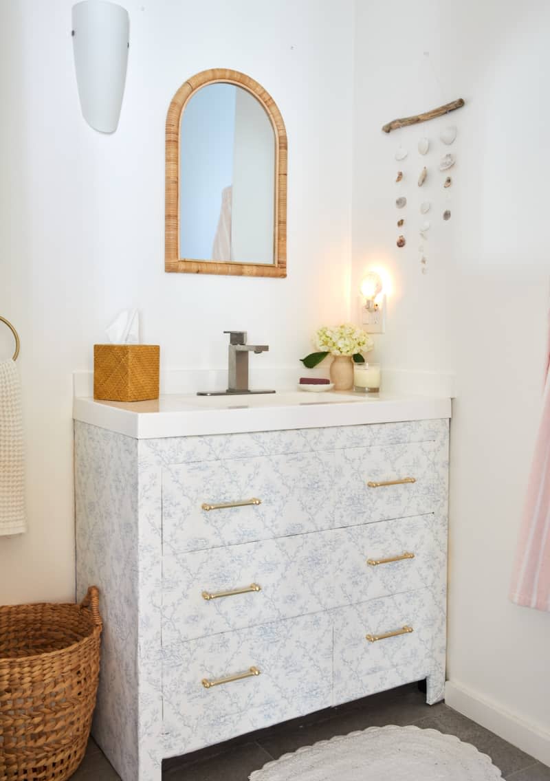 A sink base cabinet with a vinyl sticker pattern attached with golden handles in a white bathroom.