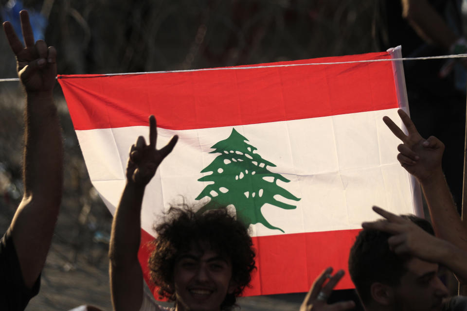 Anti-government protesters make victory signs in front of a Lebanese national flag on a road that leads to the Government House, during a protest in Beirut, Lebanon, Tuesday, Oct. 22, 2019. Prime Minister Saad Hariri briefed western and Arab ambassadors Tuesday of a reform plan approved by the Cabinet that Lebanon hopes would increase foreign investments to help its struggling economy amid wide skepticism by the public who continued in their protests for the sixth day. (AP Photo/Hassan Ammar)