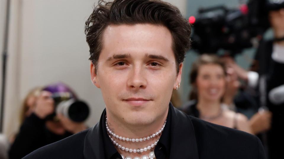 brooklyn beckham wearing a black suit with pearls around his neck at a fashion event