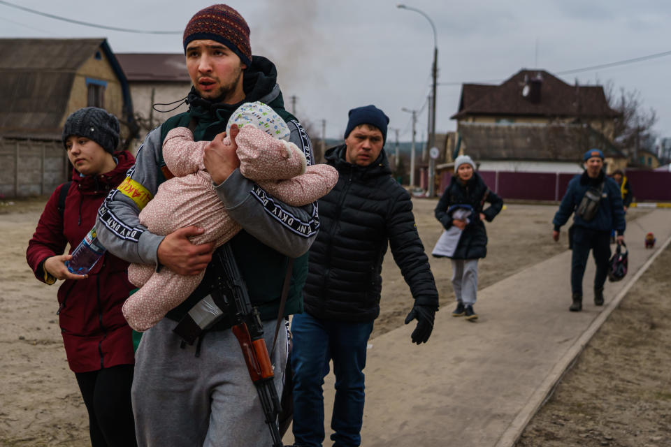 IRPIN, UKRAINE -- MARCH 6, 2022: A Ukrainian volunteer fighter helps carry a child for local residents as they evacuate on foot as Russian forces advance and continue to bombard the area with artillery, in Irpin, Ukraine, Sunday, March 6, 2022. (MARCUS YAM / LOS ANGELES TIMES)
