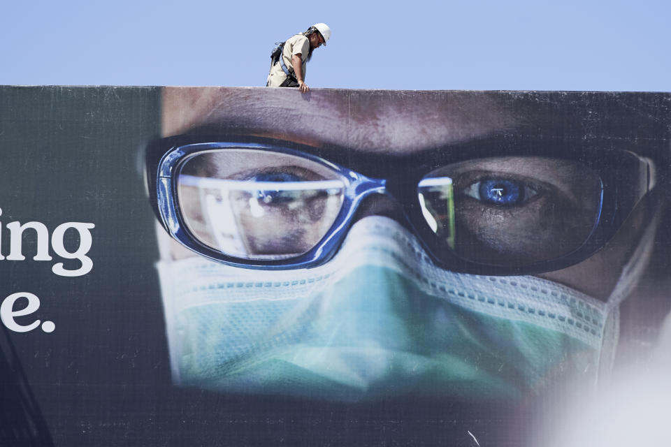 A worker stands atop a billboard showing a medical worker wearing a mask, in Omaha, Neb., Monday, July 27, 2020. Nebraska's online virus tracker on Monday showed 800 cases were confirmed Friday through Sunday, bringing the state's total to 24,618 since the outbreak began. That included 356 cases confirmed on Friday, 221 on Saturday and 223 on Sunday. (AP Photo/Nati Harnik)