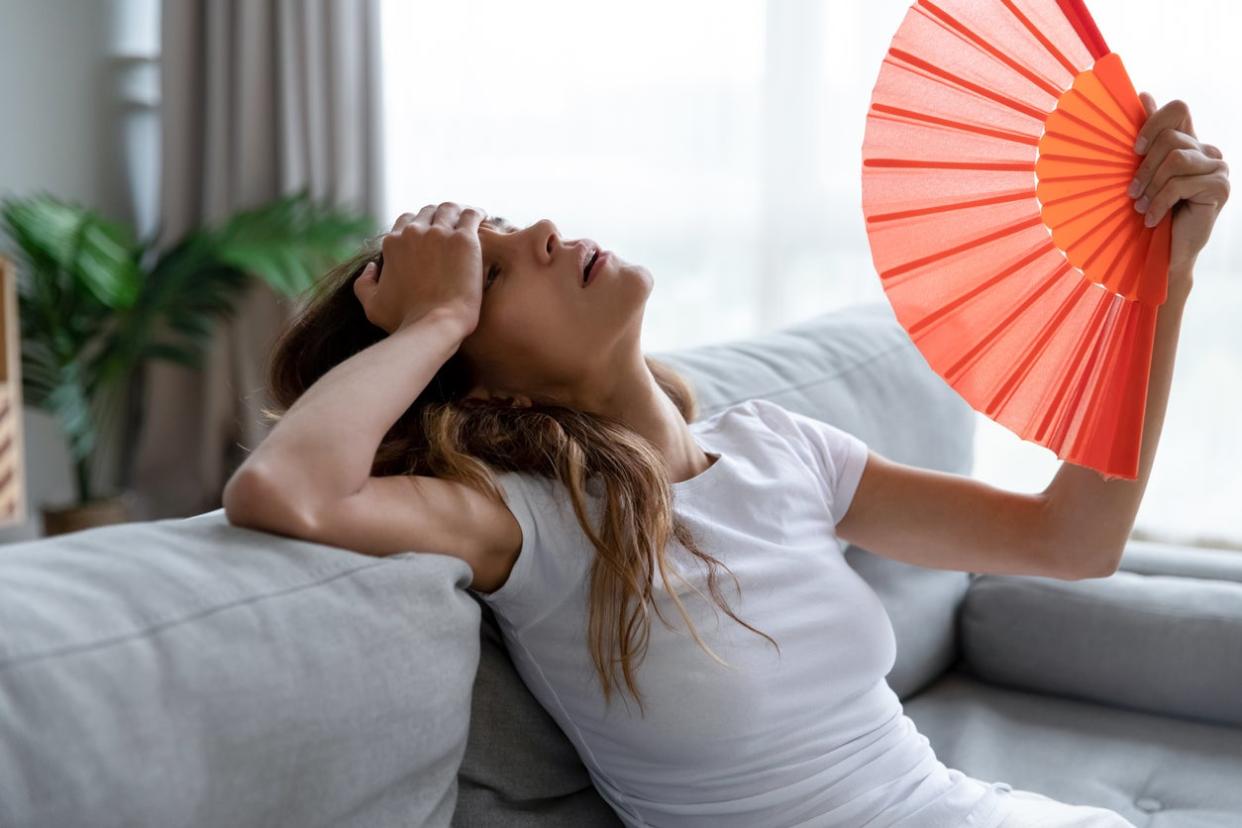 Exhausted girl using paper waver, suffering from hot summer weather.