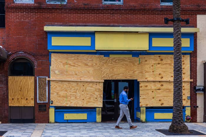 Person in business attire walks past a boarded-up storefront, checking their phone