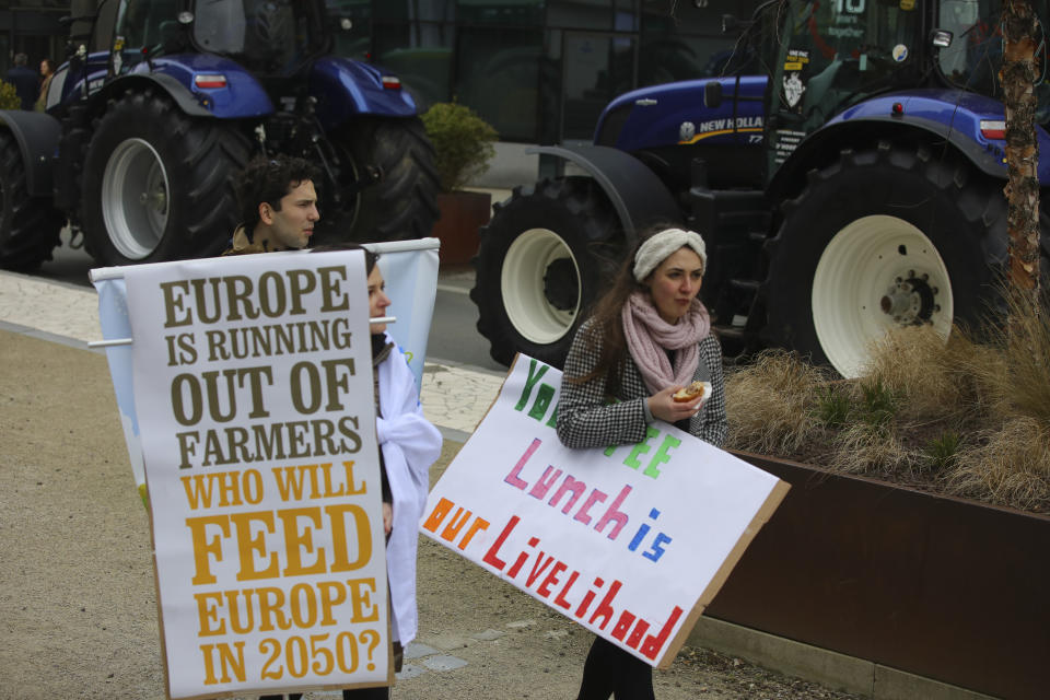 Two demonstrators walk with signs during a farmers protest outside of an EU summit in Brussels, Thursday, Feb. 20, 2020. Baltic farmers on Thursday were calling for a fair allocation of direct payments under the European Union's Common Agricultural Policy. (AP Photo/Olivier Matthys)