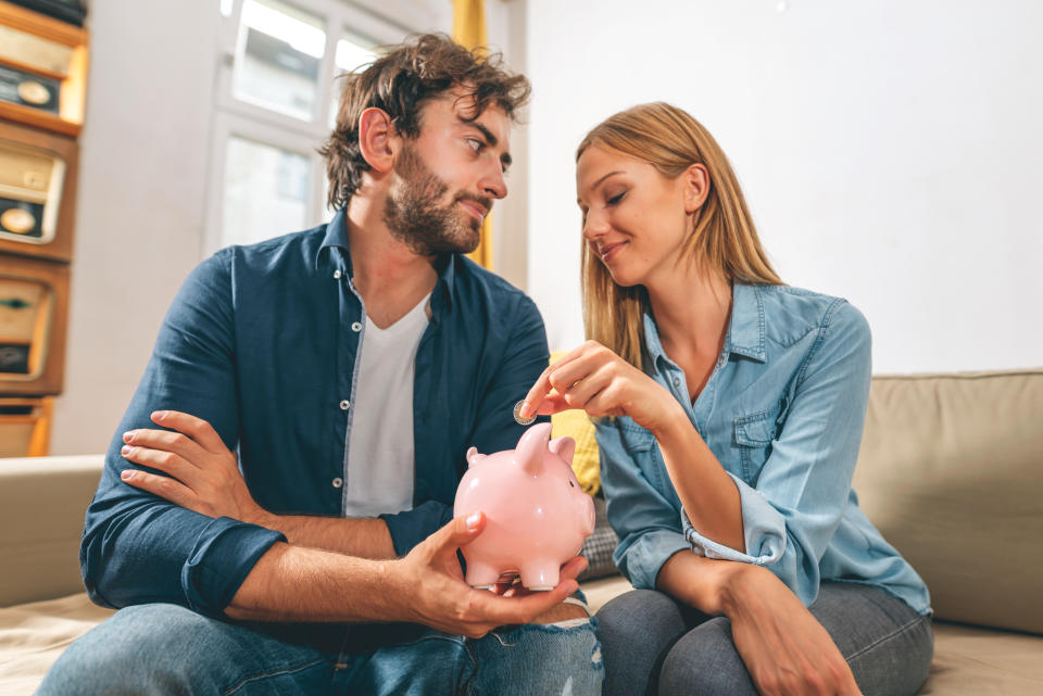 A man and a woman are sitting on a couch holding a pink piggy bank, symbolizing saving money and financial planning