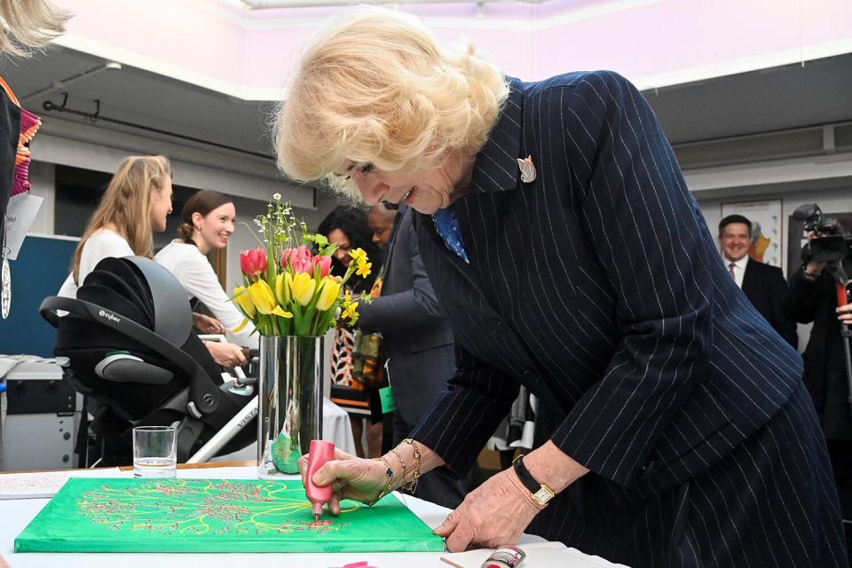 Camilla, Queen Consort, helps with a painting during a visit to the S.T.O.R.M Family Centre