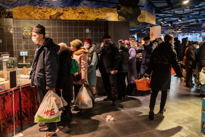 People, some at a counter, shop for food and supplies at a supermarket. 