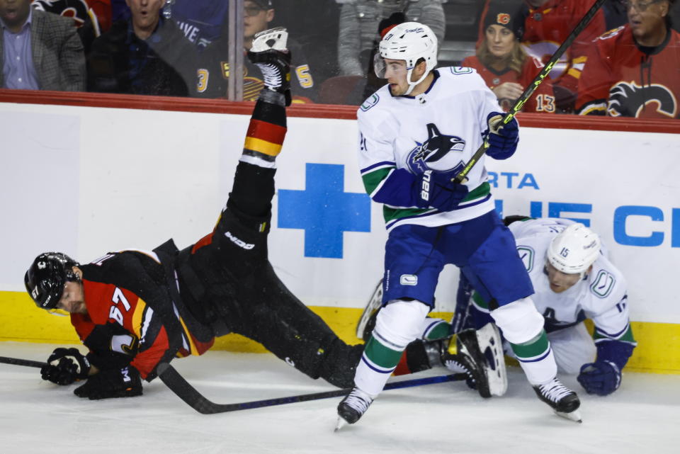 Vancouver Canucks forward Nils Hoglander, center, and forward Sheldon Dries check Calgary Flames forward Radim Zohorna during the second period of an NHL hockey game in Calgary, Alberta on Wednesday, Dec. 14, 2022. (Jeff McIntosh/The Canadian Press via AP)