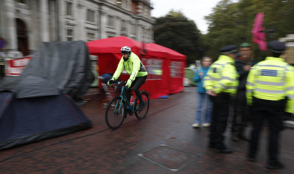 A commuter cycles past a climate change road block on the second day of ongoing protests in London, Tuesday, Oct. 8, 2019. Some protesters have set up tented villages that are disrupting normal movement of the city. Police are reporting they have arrested more than 300 people at the start of two weeks of protests as the Extinction Rebellion group attempts to draw attention to global warming. (AP Photo/Alastair Grant)