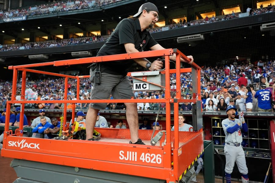 A groundkeeper moves a lift past the Los Angeles Dodgers dugout as Dodgers’ <a class="link " href="https://sports.yahoo.com/mlb/players/9552/" data-i13n="sec:content-canvas;subsec:anchor_text;elm:context_link" data-ylk="slk:Mookie Betts;sec:content-canvas;subsec:anchor_text;elm:context_link;itc:0">Mookie Betts</a>, right, cheers, in preparation to remove swarm of bees gather on the net behind home plate delaying the start of a baseball game against the Arizona Diamondbacks, Tuesday, April 30, 2024, in Phoenix. (AP Photo/Matt York)