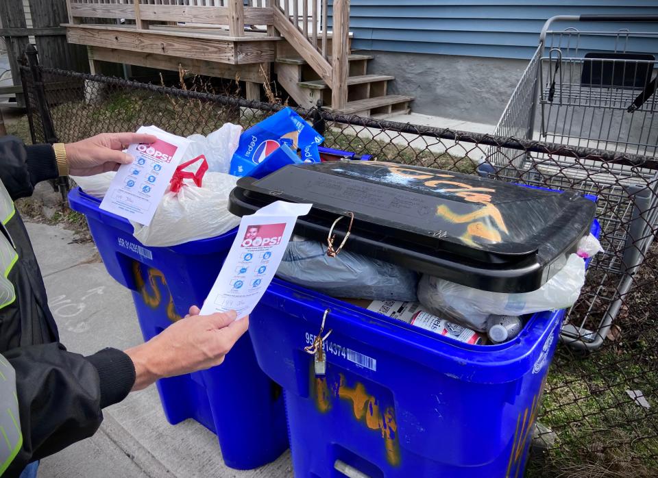 A Fall River compliance officer is seen here attaching two Oops! warning cards to recycle bins that are not in compliance with city trash collection rules.