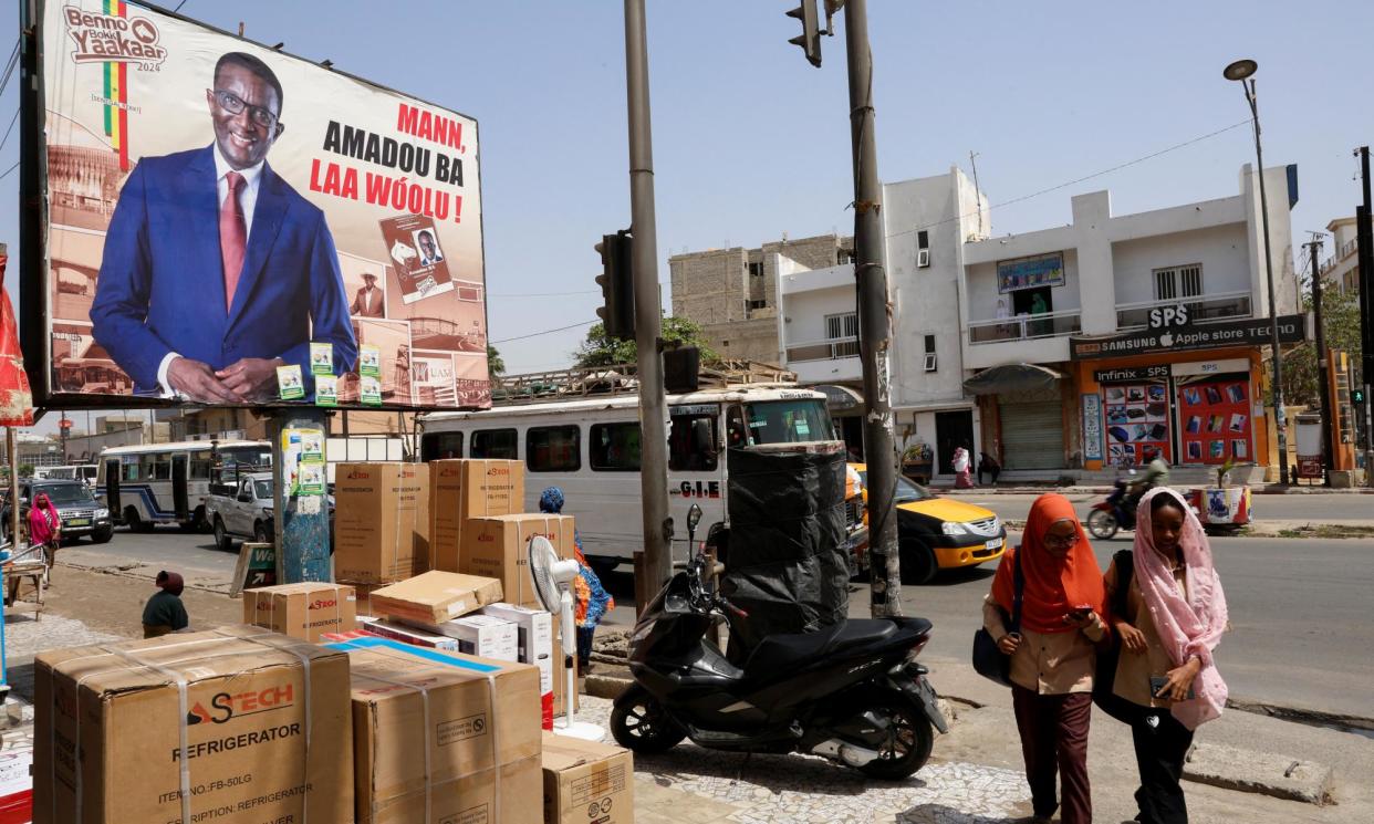 <span>People walk past an electoral billboard of candidate Amadou Ba of President Macky Sall's ruling coalition, in a street in Dakar.</span><span>Photograph: Luc Gnago/Reuters</span>