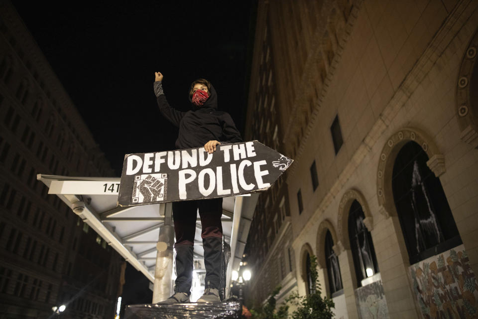 A protester holds a sign calling for the defunding of police at a protest on Saturday, July 25, 2020, in Oakland, Calif. Protesters in California set fire to a courthouse, damaged a police station and assaulted officers after a peaceful demonstration intensified late Saturday, Oakland police said. (AP Photo/Christian Monterrosa)