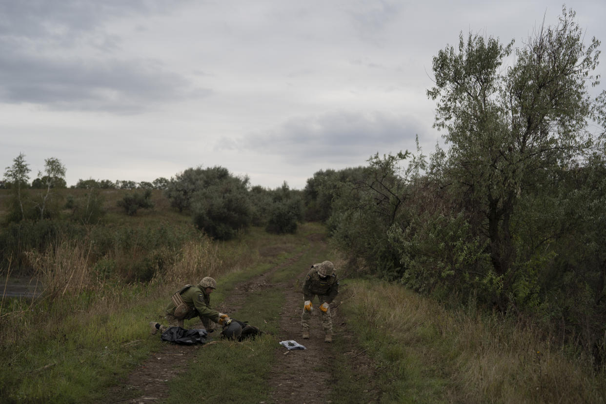 Ukrainian servicemen examine the body of a Ukrainian soldier in a retaken area near the border with Russia in Kharkiv region, Ukraine, Saturday, Sept. 17, 2022. (AP Photo/Leo Correa)