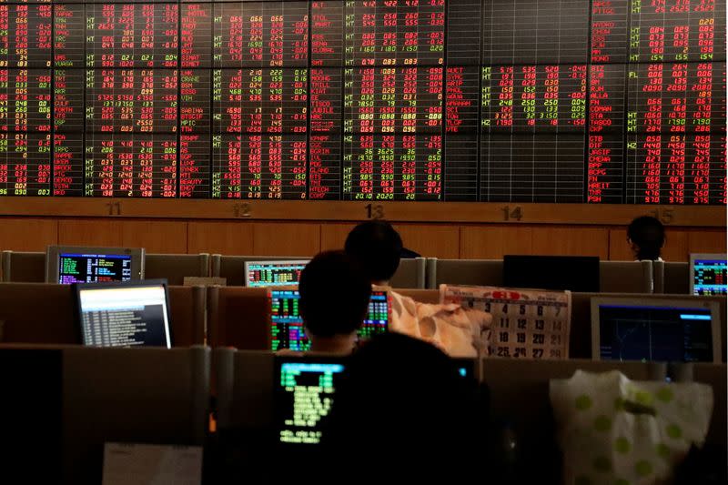 Traders are seen in front of a screen with trading figures in red at Thailand Stock Exchange building in Bangkok