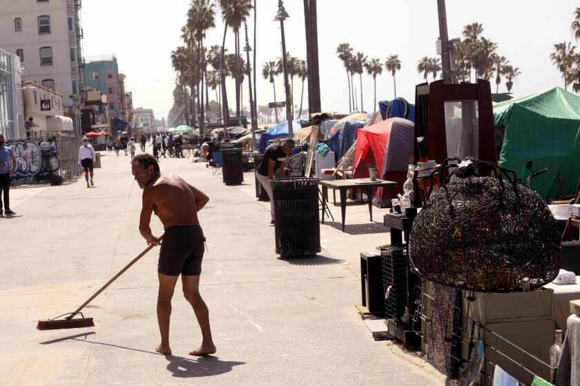 VENICE, CA - APRIL 16, 2021 - - David Cruz, 55, who is homeless, sweeps up Ocean Front Walk near a row of homeless encampments in Venice on April 16, 2021. (Genaro Molina / Los Angeles Times)
