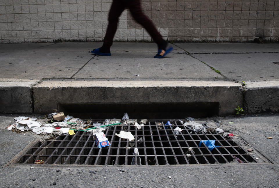 In this Monday, May 25, 2020 photo a person walks past a storm drain with discarded gloves and other trash in Philadelphia. Between mid-March, when the city’s stay-at-home order was issued, and the end of April, most of the 19 sewer and storm water pumping stations in Philadelphia had experienced clogs from face masks, gloves and wipes residents had pitched into the potty, Philadelphia Mayor Jim Kenney said.(AP Photo/Matt Rourke)