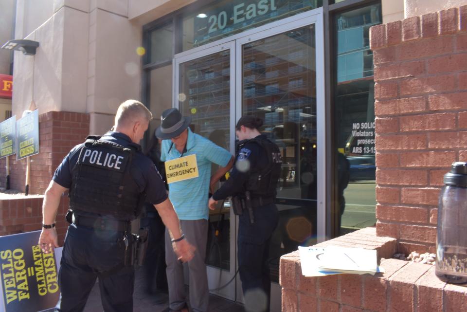 Police officers arrest Troy Horton for trespassing. Horton tied himself to the front doors of a building in Tempe that houses a Wells Fargo branch to protest the bank's financing of fossil fuels emissions.