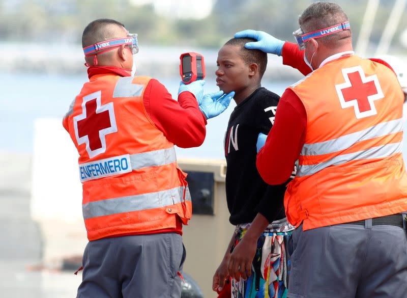 FILE PHOTO: Red Cross members take the temperature of a migrant before disembarking from a Spanish coast guard vessel in the port of Arguineguin on the island of Gran Canaria