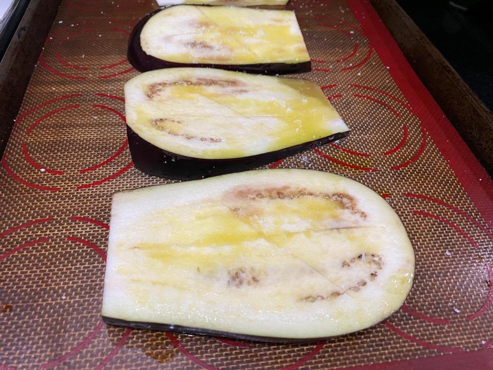 Three slices of raw eggplant laid out on a baking sheet.