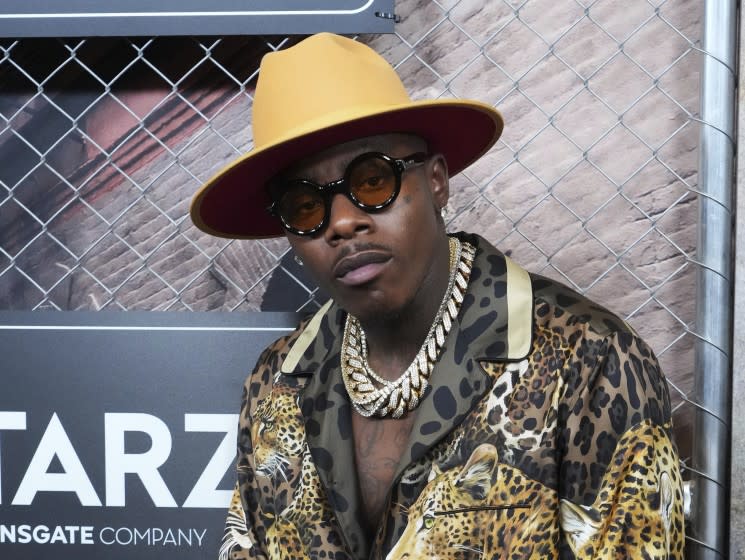 A man in a hat, glasses, gold chains and an animal-print jacket