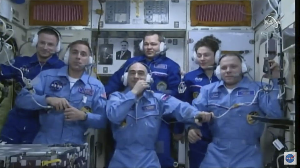 In this image from video made available by NASA, newly-arrived International Space Station crew members, foreground from left, Chris Cassidy, Anatoly Ivanishin and Ivan Vagner, stand with outgoing crew members, background from left, Andrew Morgan, Oleg Skripochka, and Jessica Meir during a news conference on Thursday, April 9, 2020. (NASA via AP)