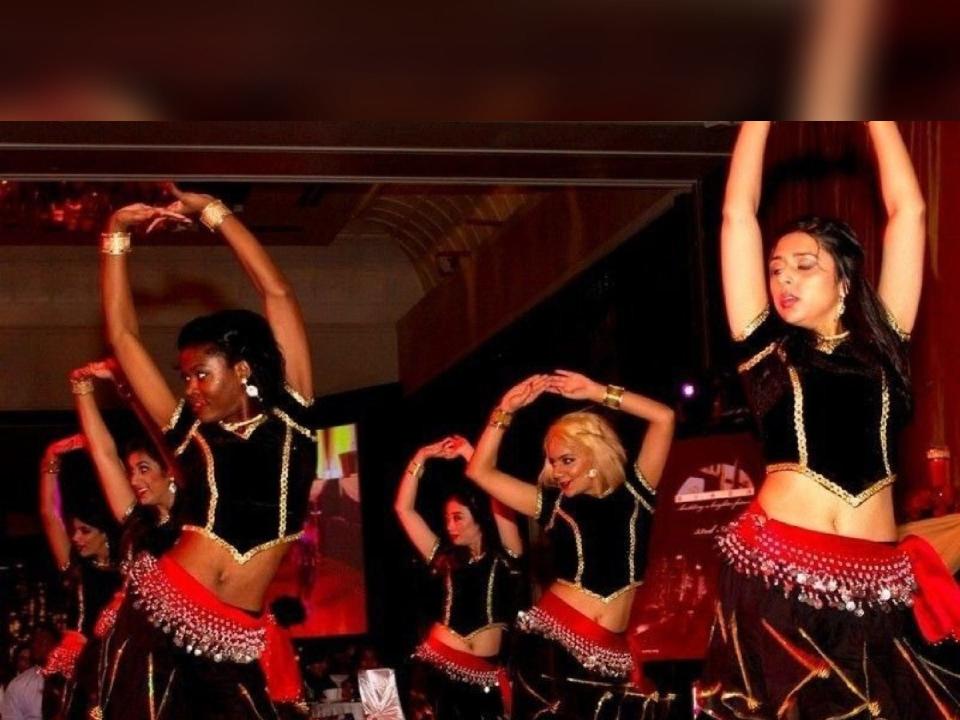 Sonali Chandra, wearing traditional Indian dress, performs a Bollywood-style dance with five other women.