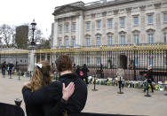 Two people stand behind a barrier as they view flower tributes left in front of the gate at Buckingham Palace in London, a day after the death of Britain's Prince Philip, Saturday, April 10, 2021. Britain's Prince Philip, the irascible and tough-minded husband of Queen Elizabeth II who spent more than seven decades supporting his wife in a role that mostly defined his life, died on Friday. (AP Photo/Alberto Pezzali)