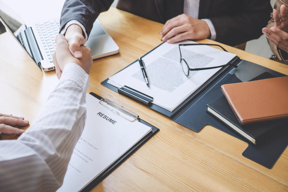 Midsection Of Employer Giving Handshake To Candidate In Office